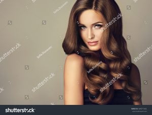 Woman with long, wavy brown hair styled elegantly, looking directly at the camera with a neutral expression.