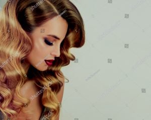 Profile view of a woman with long, wavy blonde hair and makeup, looking down.