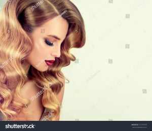 Woman with long, wavy blonde hair styled elegantly, looking down with a soft expression.