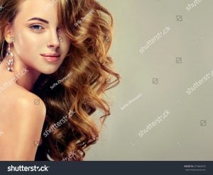 Woman with long, curly hair and dangling earrings, looking over her shoulder with a subtle smile.