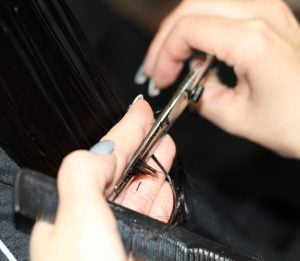 Close-up view of a hairdresser's hands using scissors to trim dark hair, with a comb present, at HeadStart Exeter hairdressers & salon