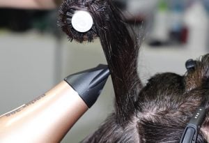 Dark hair being styled in HeadStart Exeter salon using a round brush and handheld dryer close to the scalp, professional hairdressing tools visible.