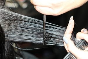 Close-up of a hairstylist cutting long black hair with scissors and a comb in a hair salon, HeadStart Exeter