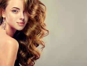 Woman with long, wavy hair and earrings, posing with a soft expression against a neutral background.