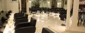 Interior view of HeadStart Exeter hair salon showing a row of black styling chairs beside mirrors, a bright white tiled floor, and shelving in the background
