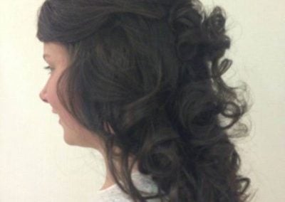 Side view of a woman with a voluminous curly hairstyle featuring defined curls and layered texture.