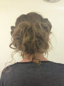 Back view of a styled updo with loose curls and twists in brown hair.