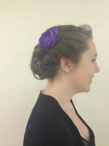A woman with a side profile hairstyle adorned with a purple flower accessory in her hair.