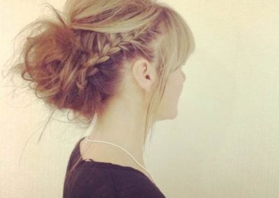 A side view of a woman with an elegant updo hairstyle featuring braids and loose curls.