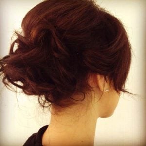 A woman with a dark brown elegant updo hairstyle, showcasing soft curls and a side view of her head.