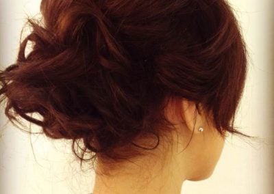 A woman with a dark brown elegant updo hairstyle, showcasing soft curls and a side view of her head.