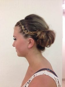 Side view of a woman with a braided updo hairstyle featuring a side braid and loose curls.