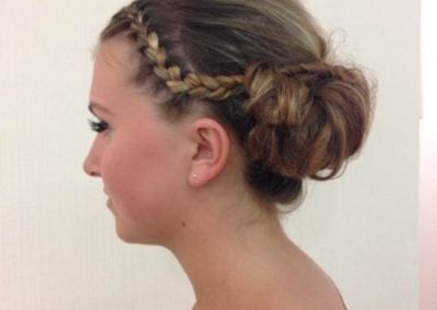 Side view of a woman with a braided updo hairstyle featuring a side braid and loose curls.
