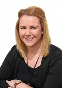 Woman with blonde hair and a black top smiling at the camera with arms crossed.