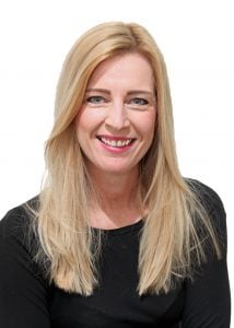 Smiling woman with long blonde hair wearing a black top, against a white background.