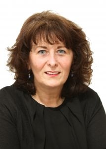 Woman with curly brown hair and blue eyes wearing a black top, looking directly at the camera.