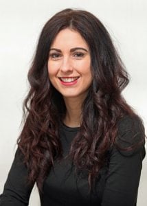 Woman with long, curly dark hair and a black top smiling at the camera.