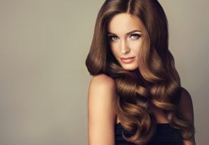 A model with long, wavy brown hair styled elegantly, looking directly at the camera.